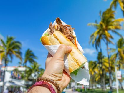 A hand holding up a Cuban sandwich to the clear skies of Miami, Florida