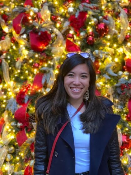 A Hilton Grand Vacations Member posing in front of a glittering Christmas tree while visiting New York
