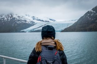 Woman gazing at water, snowcapped mountains, winter skies, Alaska cruise vacation. 