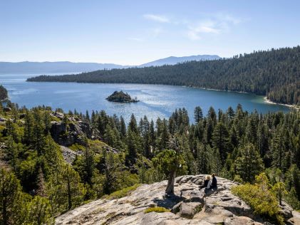 Hikers sit on a rock overlook of South Lake Tahoe on a sunny day
