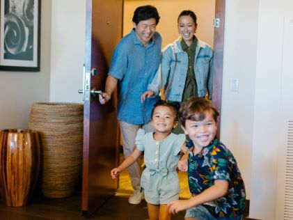 Two children excitedly run into their Suite at The Grand Islander, a Hilton Grand Vacations Club in Oahu, Hawaii, with their parents in tow
