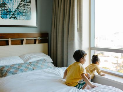 Two kids stare out the Suite window from the bed at The Grand Islander, a Hilton Grand Vacations Club in Oahu, Hawaii