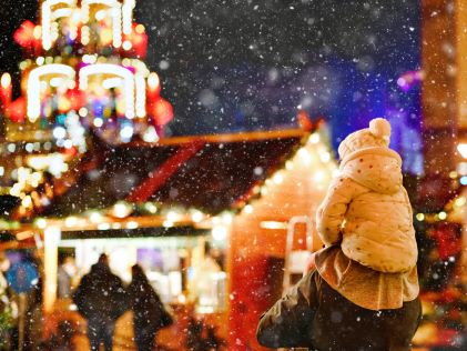 A little girl rides on her dad's shoulders while looking at holiday lights in the snow