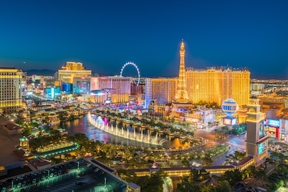 Long shot of the Las Vegas Strip just after dusk. Bright lights and attractions dot the skyline with a warm glow.