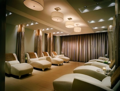 Interior photo of The Boulevard, a Hilton Grand Vacations Club eforea spa. An inviting spa area with multiple lounge seats. Warm and soft lighting throughout with dramatic drapes in the background.