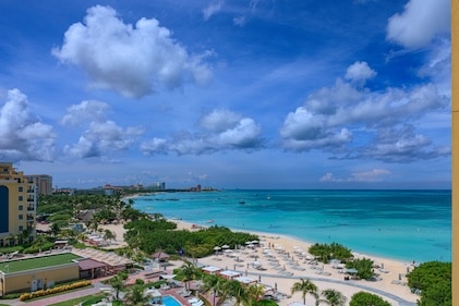 The sun has just risen over the tourist resort of Palm Beach in Aruba on the South Caribbean Sea. Several hotels and boats at anchor are seen in the image. There however, is hardly anyone on the beach as yet. Obviously it is too early. The sea is very calm. In the horizon, is an oil drilling rig. There are a few people in the image but they are too far away to be recognised. Photo shot in the early morning sunlight;.