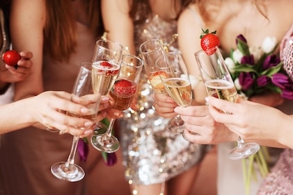 Closeup of women's hands as they Lift glasses of champagne in bachelorette party celebration. Each glass has a single strawberry.