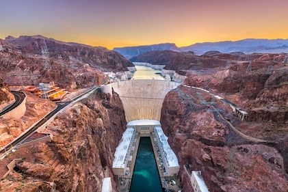 Drone shot of the Hoover Dam straddling Nevada and Arizona. The sun sets in the distance and blue waters can be seen flowing from the dam below.