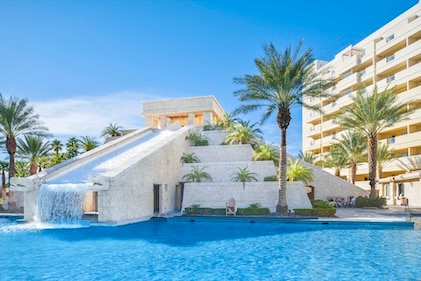 Daylight image of the Aztec-inspired pool fountain at Cancun Las Vegas, a Hilton Vacation Club, featuring crystal blue waters below and clear blue sky above.