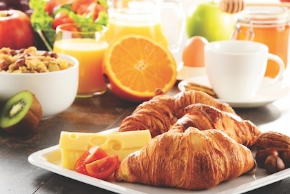 Close up of a brunch setting with croissants, cheese and coffee. A ripe cut orange and other colorful food items fill the background.