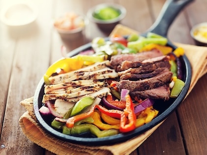 Closeup of fajita plate adorned with colorful peppers, avocado, seared chicken and steak.