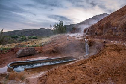 Outdoor hot spring tub, steaming, desert red rocks, muted winter skies overhead, Mystic Hot Springs, Monroe, Utah. 