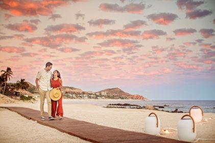 Idyllic romantic scene, couple embracing along boardwalk, calm golden shore and Sea of Cortez in the distance, cotton candy painted skies overhead, Los Cabos, Mexico. 