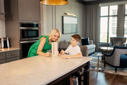 Woman and young kid playing board game, spacious Suite kitchen, Liberty Place Charleston, a Hilton Club, South Carolina. 