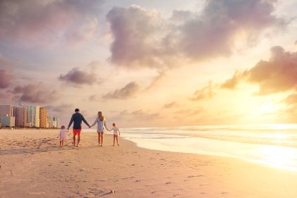 Family walking along golden shoreline, sunrise glowing sky, calm waters, Myrtle Beach, South Carolina. 