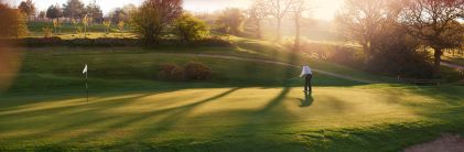 Golfer on green, early morning mist.