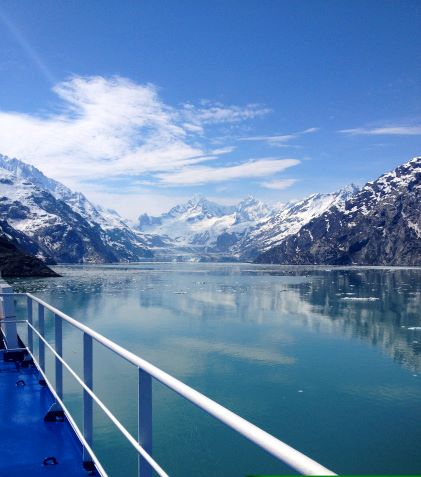 Point of view image, overlooking ocean from cruise, snow capped mountains against clear blue skies.