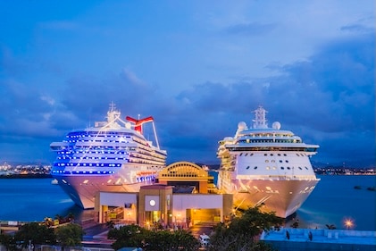 Bow facing forward on two cruise ships side by side in port under night skies with the lights glowing a golden color.