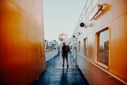 Man with carry-on backpack on narrow decking between two large, orange ships imposing on either side.